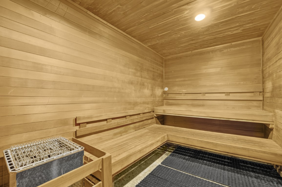 Novus Wood-paneled sauna room with tiered bench seating, a heater on the left, and mats on the floor under warm ceiling lighting.