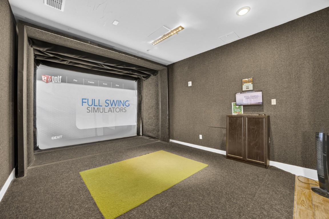 Novus Indoor golf simulator room with a large projection screen, green mat, and brown carpeted walls and floor.