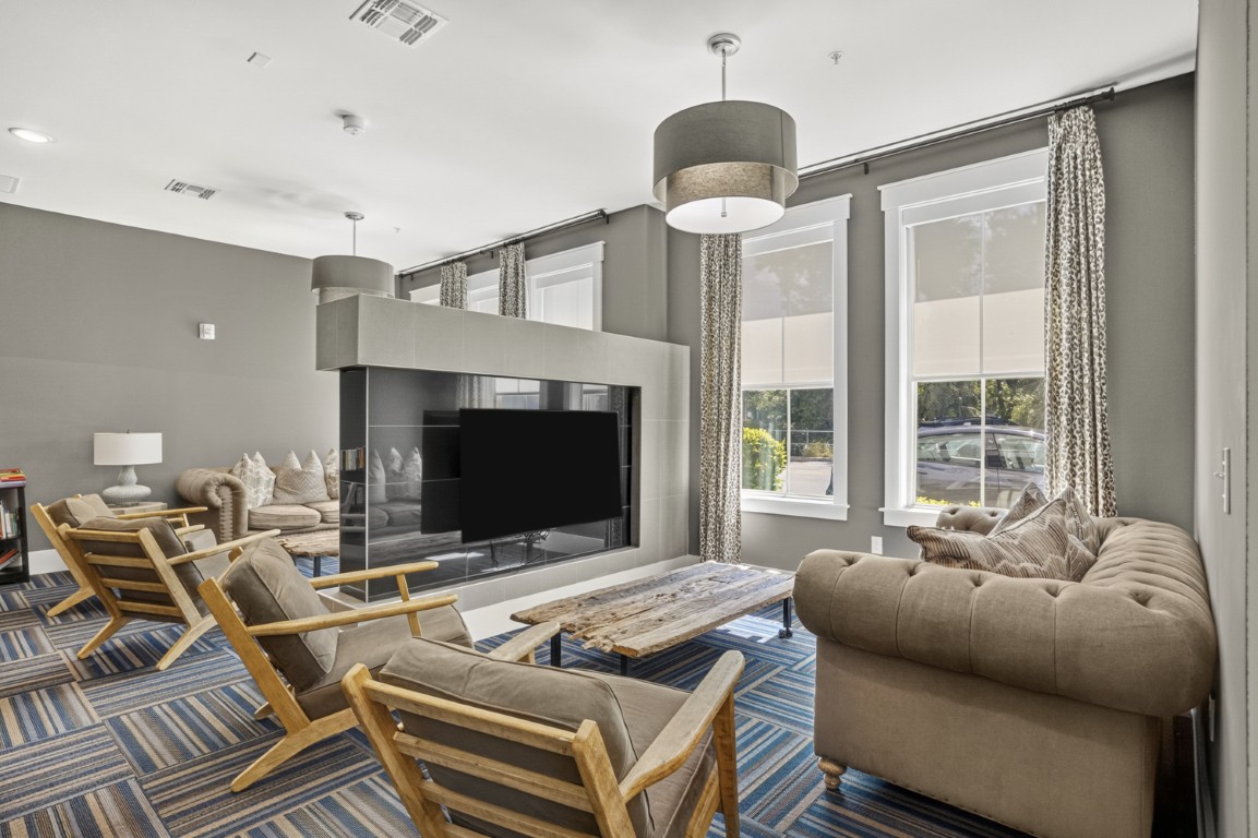 Novus Modern living room with beige sofas, wooden chairs, striped carpet, large windows, and a TV mounted on a central wall.