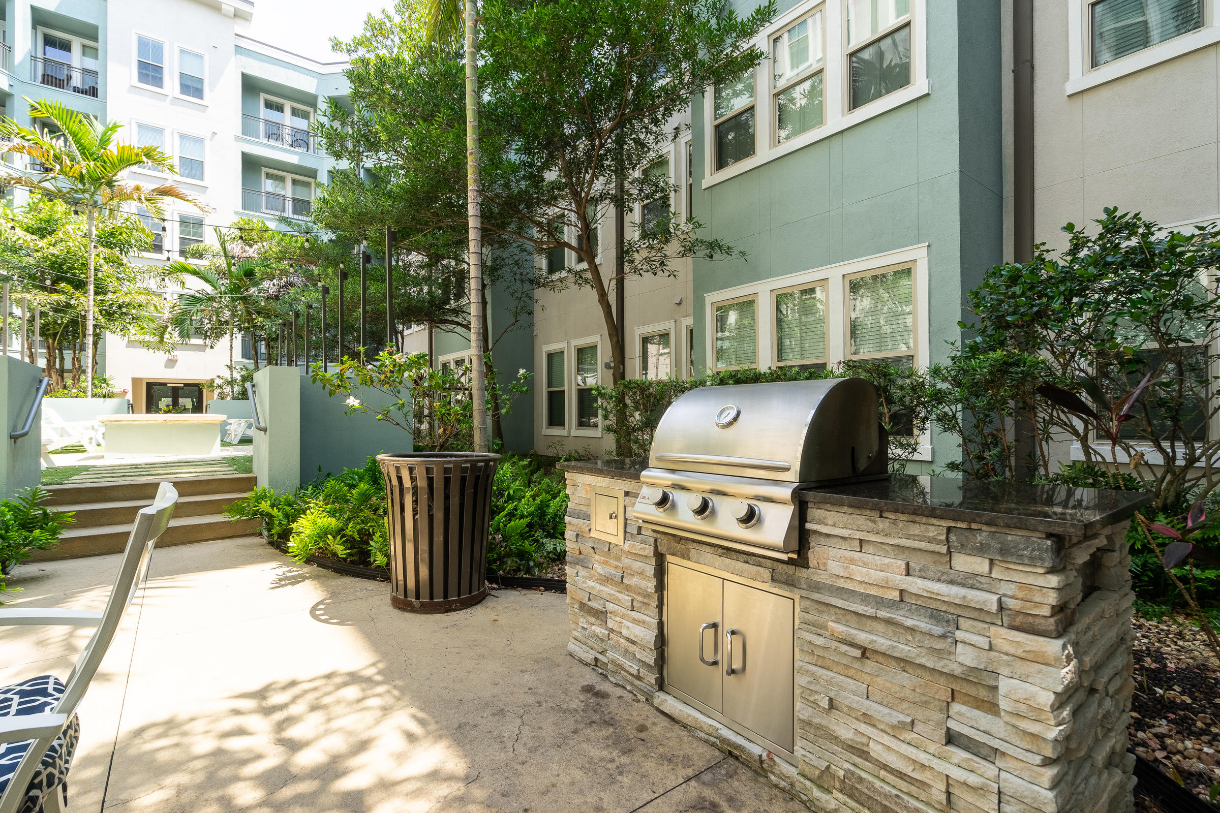 Outdoor grill and seating area in a modern apartment courtyard with greenery and surrounding buildings.