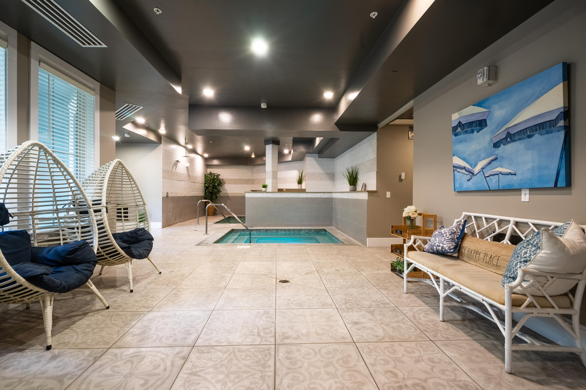 Indoor spa area with a small pool, lounge chairs, and modern decor under bright lighting.