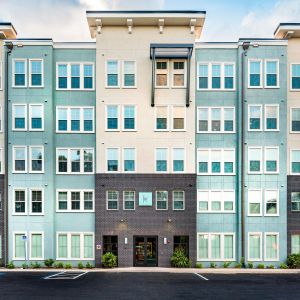 Modern apartment building with multiple windows, pastel colors, and a palm tree on the right side.