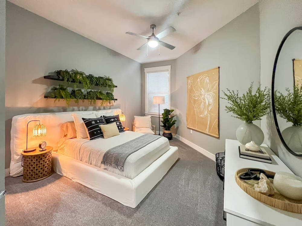 Modern bedroom at Novus Westshore with a white bed, indoor plants, soft lighting, and minimalist decor—your best place to live in Westshore Tampa.