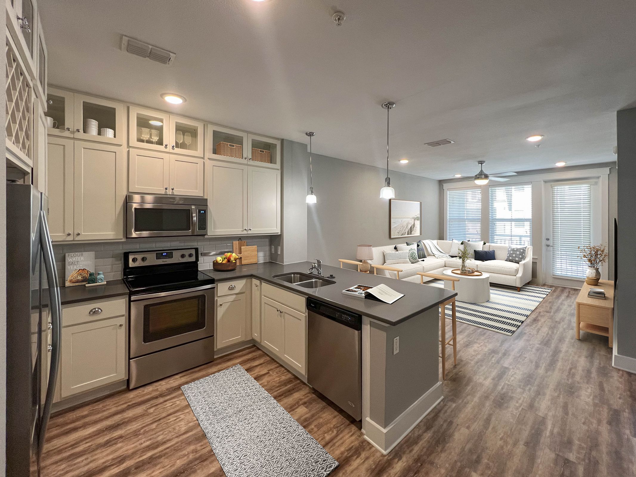 Novus Modern open-concept kitchen and living room with stainless appliances, white cabinets, and wood flooring.