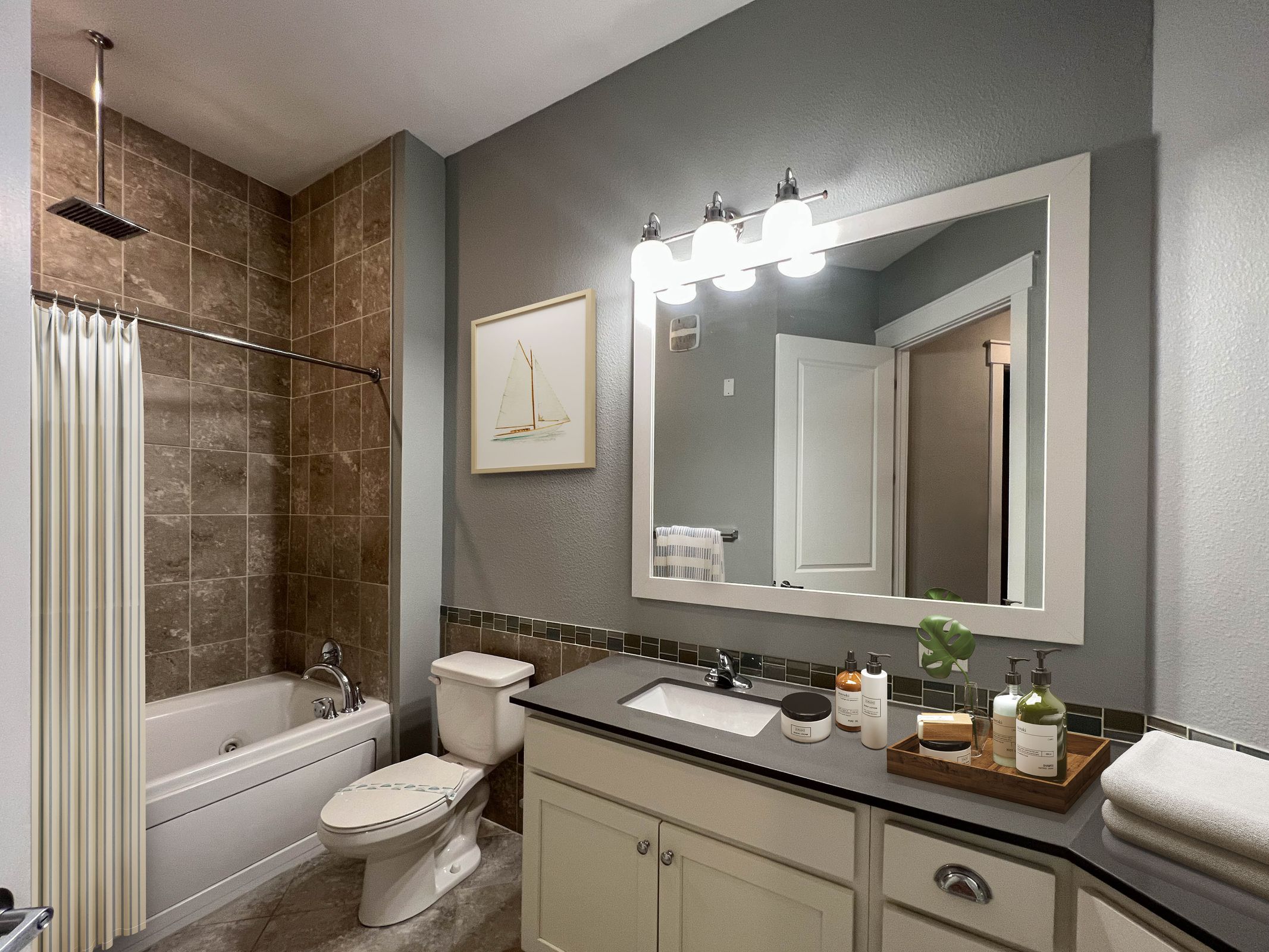 Novus Modern bathroom with gray walls, a bathtub with brown tiles, a large mirror, and a white sink with toiletries on the counter.