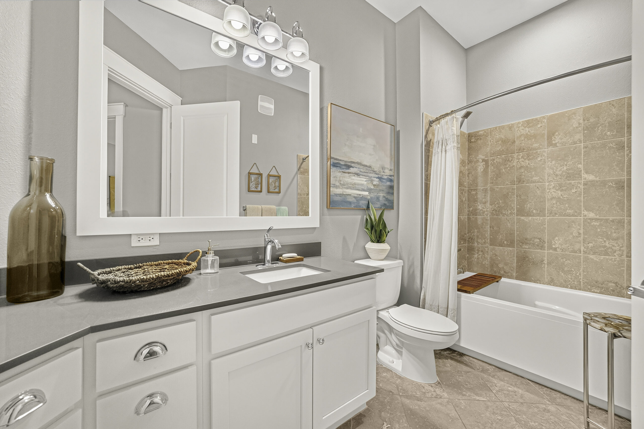 Novus Modern bathroom with white cabinets, gray countertop, a large mirror, and a tiled shower-bathtub with a curtain and simple decor.