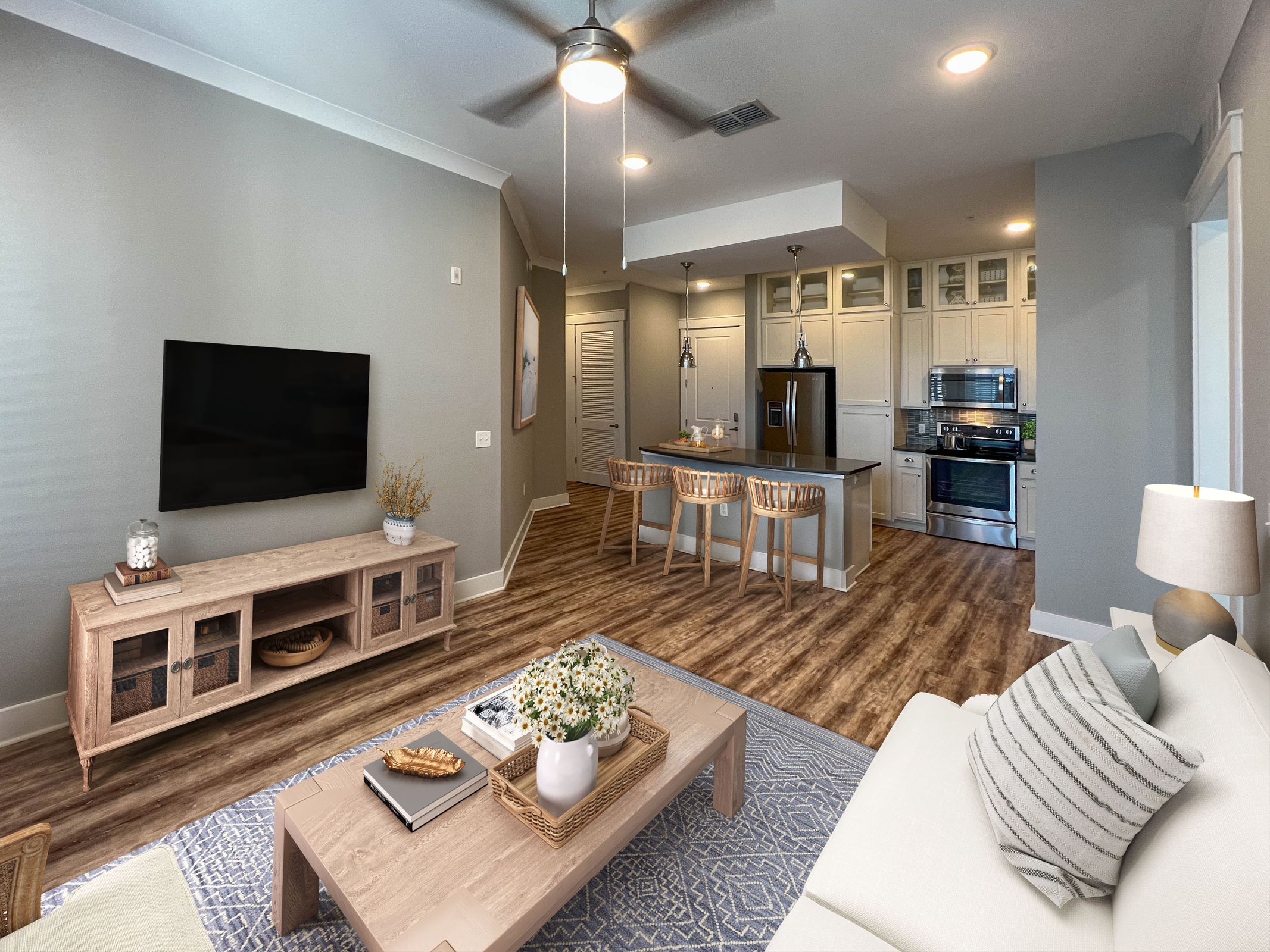 Novus Modern living room and kitchen with wood floors, light furniture, TV, bar stools, and stainless steel appliances.