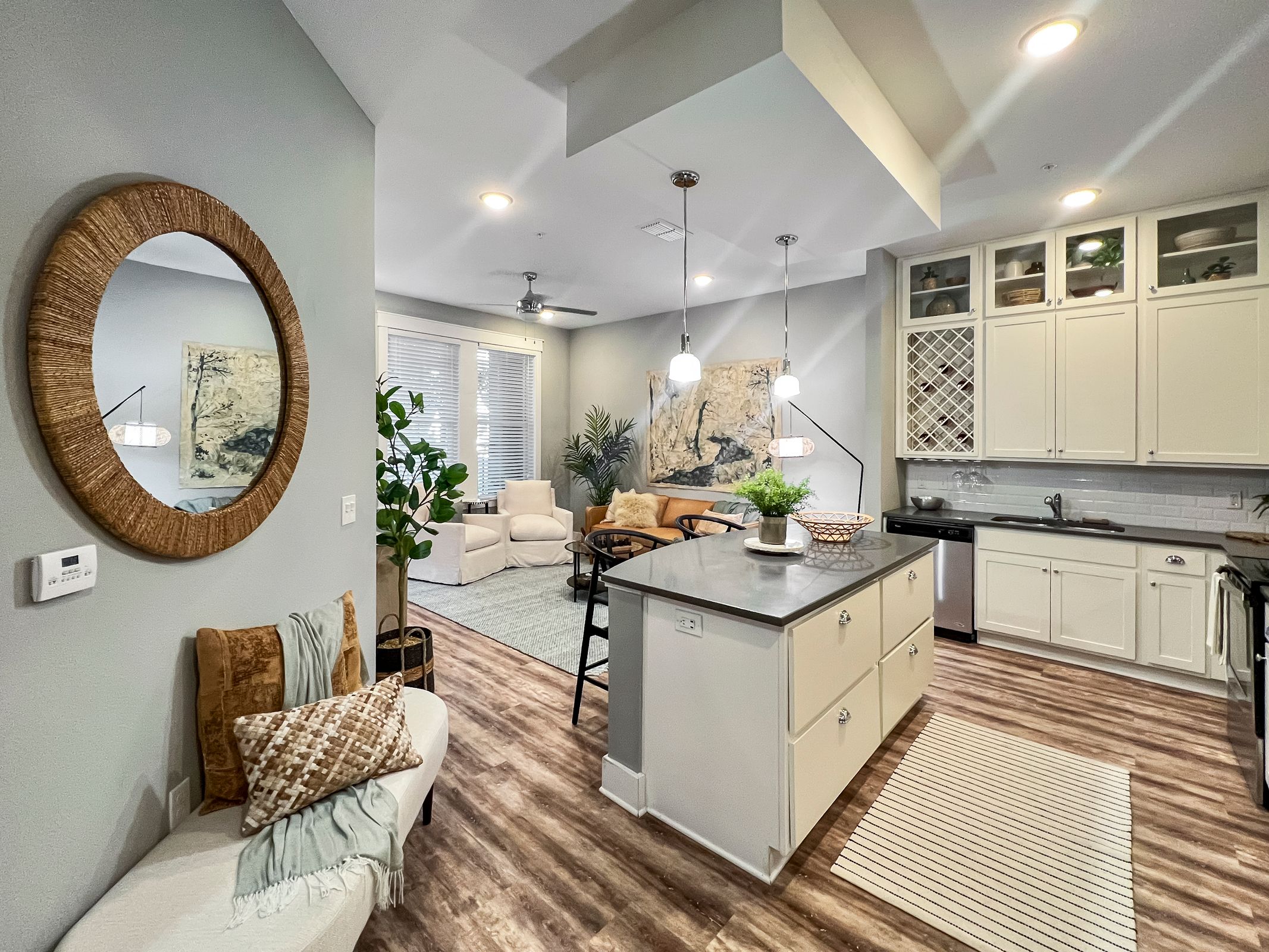 Novus Open-concept kitchen and living room with island, modern decor, round mirror, plants, and large windows letting in natural light.