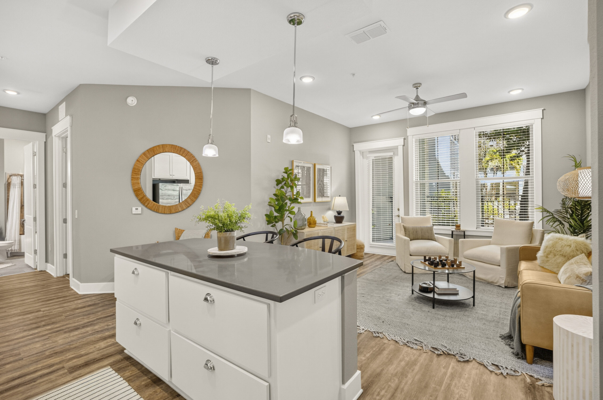 Novus Modern living room and kitchen with white island, cozy seating, plants, and large windows letting in natural light.
