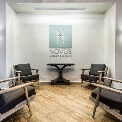 Modern lounge with four armchairs around a small table, Novus Westshore logo on wall, wood flooring.