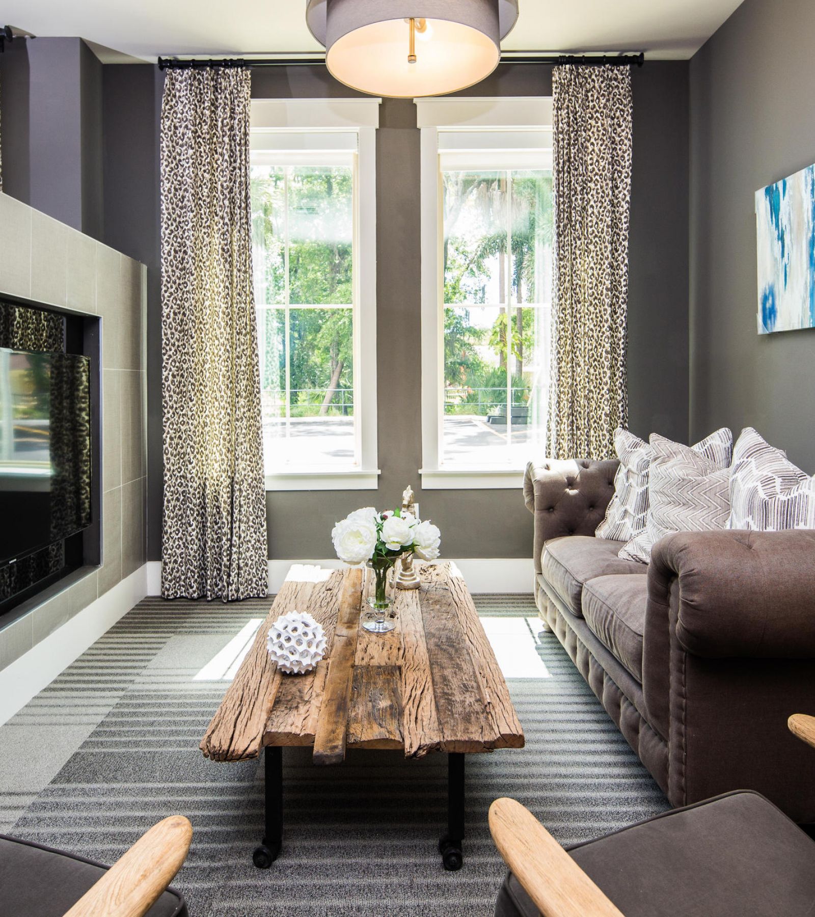 Modern living room with gray walls, patterned curtains, a brown sofa, and a rustic wooden coffee table.