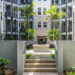 Modern apartment courtyard with palm trees, string lights, and a ping pong table at the center.